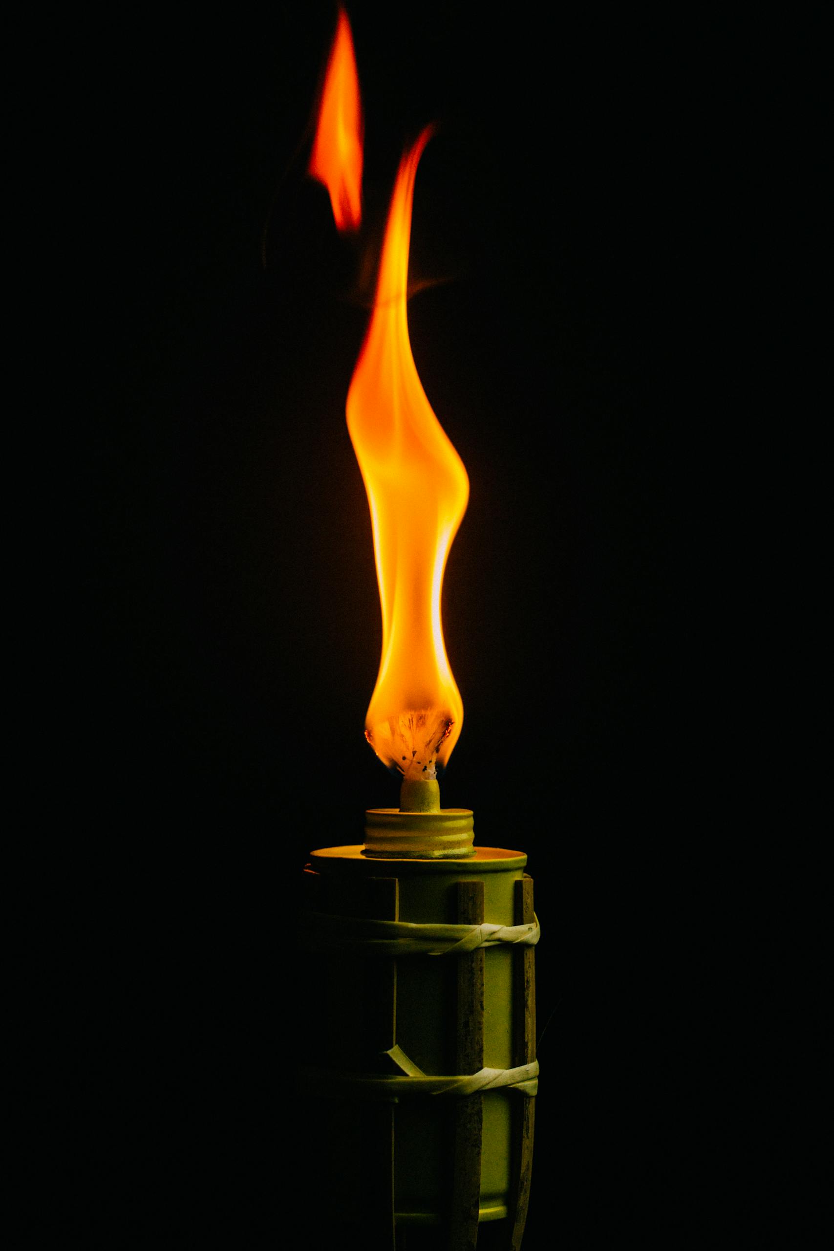 Close-up of a lighted torch with orange flame against a black background.